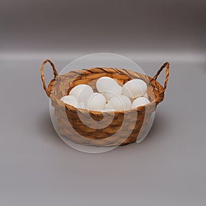 White chicken eggs in a brown wicker basket on a gray background