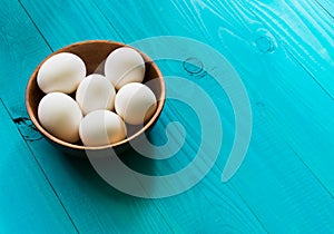 White chicken eggs in a brown wooden bowl on a turquoise background