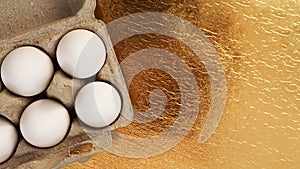 White chicken eggs in a cardboard tray on a gold background