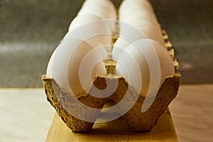 White chicken eggs in the cardboard on wooden surface with interesting light. Fresh eggs from the farm. Organic egg production.