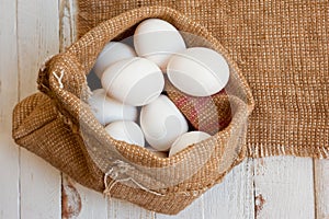 White chicken eggs lying in a canvas bag, shot on a white painted wooden surface. Background for livestock products