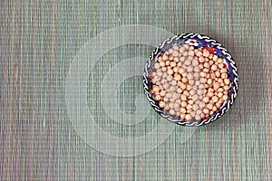 White chickpeas or Turkish pea Cicer arietinum, in a round ceramic cup, standing on a straw mat, top view