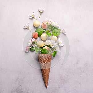 White chocolate truffle candy flowers waffle cone ice cream on gray concrete background. Square frame copy space.