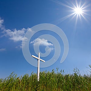 White christian cross stay on green grass hill under a sparkle sun