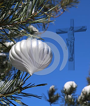 White Christmas ball on real live outdoor Christmas tree with semi-transparent crucifix