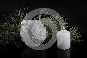 White Christmas ball and white candle with fir twig on black background