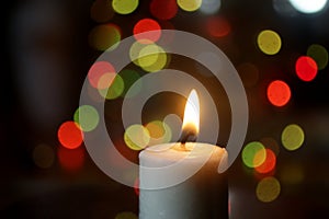 White Christmas candle light on the table. On beautiful background of colorful bokeh lights decoration.