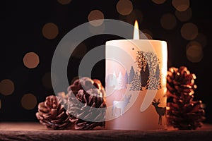 White Christmas candle and small brown pine cones on a wooden table with garlands background