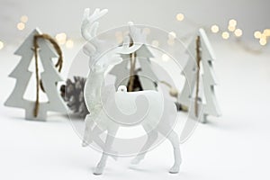 White Christmas decoration in scandinavian style with reindeer, wood fir trees and pine cones, bokeh lights in the background