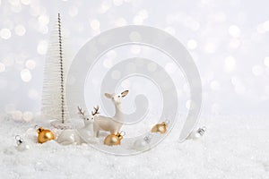 White Christmas greeting card. Two reindeer in snow on white background with golden baubles, Christmas tree and bokeh lights.