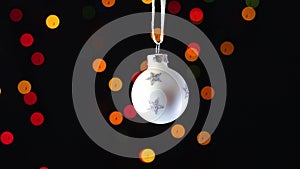 White Christmas ornament with glitter stars swing with blinking lights behind