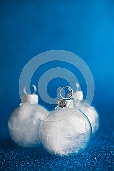 White christmas ornaments on dark blue glitter background with space for text.