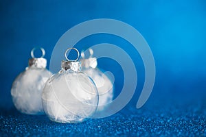 White christmas ornaments on dark blue glitter background with space for text.