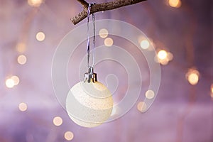 White Christmas Tree Ball Hanging on a Branch Golden Garland Glittering Lights in the background Festive Greeting Card