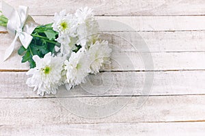 White chrysanthemum bouquet with silk ribbon lies on white wooden table