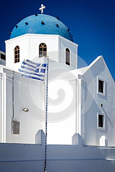 White church with blue dome and Greek flag, Santorini