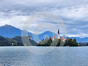 white church on island on lake Bled. Dark blue mountains. Slovenia. Europe