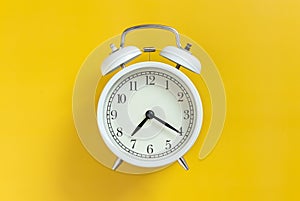 white circle retro classic analog alarm clock with clock needle isolated on yellow empty background with copy space.