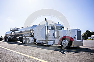 White classic big rig semi truck with tank semi trailer for transporting liquid cargo standing on truck stop parking lot