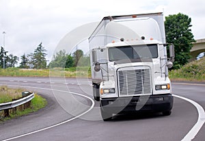 White classic big rig semi truck with trailer turning out from g