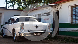 A white classic car parked front of house