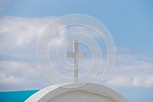 White classic cross, blue sky with white clouds in the background. Religion, faith and prayer concept