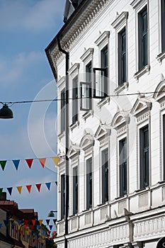 A white classic old facade with windows open towards the street decorated with colorful flags in the city of Lund, Sweden