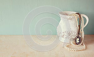 White classic victorian vase on wooden table with a collection of romantic vintage jewelry and pearls. retro filtered image. room