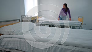 White clean bedding in hospital ward with blurred young woman making bed at background leaving. Unrecognizable Caucasian