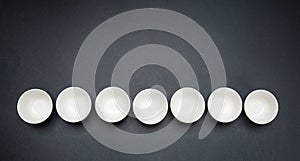 White clean ceramic bowls in a row, black background, copy space, top view