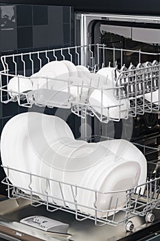 White, clean cups and plates in an open dishwasher