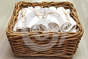 White clean rolled terry towel stack in wicker basket on natural wooden background. Close up