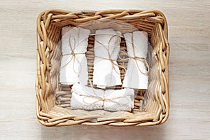 White clean rolled terry towel stack in wicker basket on natural wooden background. Flat Lay