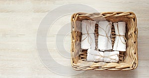 White clean rolled terry towel stack in wicker basket on natural wooden background. Flat Lay