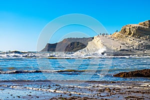 White cliffs naturally made of smooth pug at Scala dei Turchi beach full of people with stormy mediterranean sea, Sicily, Italy