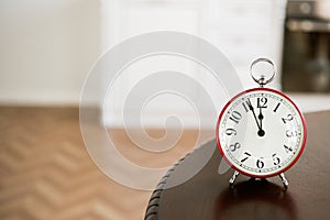 White clock in a red outline show time stands on a dark table in the room