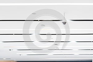 White Closed circuit television CCTV is hung on a white ceiling beside the air vents