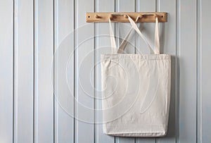 a white cloth bag is hanging on a wooden hanger on a white wall.