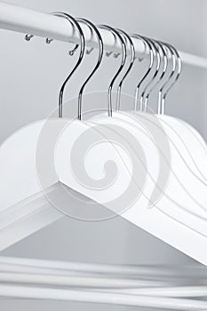 White clothes hangers on metal rail against light background, closeup