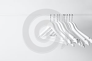 White clothes hangers on metal rail against light background. Space for text