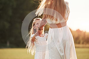 In white clothes. Mother and daughter enjoying weekend together by walking outdoors in the field. Beautiful nature