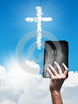 White cloud Christian cross and hand with Bible photo