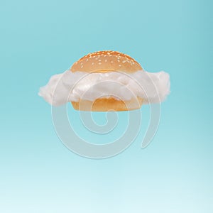 White cloud inside hamburger bun floating against blue sky background. Surreal fast food concept.