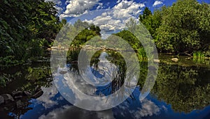 White clouds in the blue sky are reflected in the river.