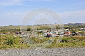 White clouds in the bright blue summer sky over village with small houses far away in the mountains and fields. Travelling. Peopl