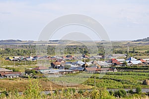 White clouds in the bright blue summer sky over village with small houses far away in the mountains and fields. Travelling. Peopl