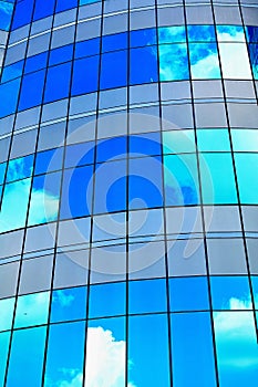 White clouds reflect sunlight on tall glass blue abstract crop of modern office skyscraper texture and bacgound.