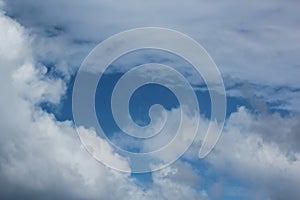 White clouds of various shapes against the blue sky and the sun above the surface of the ocean.