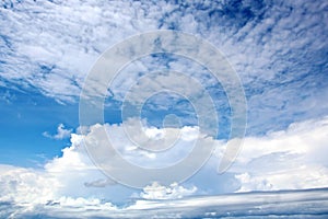 White clouds of various shapes against the blue sky and the sun above the surface of the ocean.