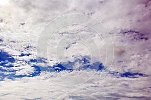 White clouds of various shapes against the blue sky and the sun above the surface of the ocean.